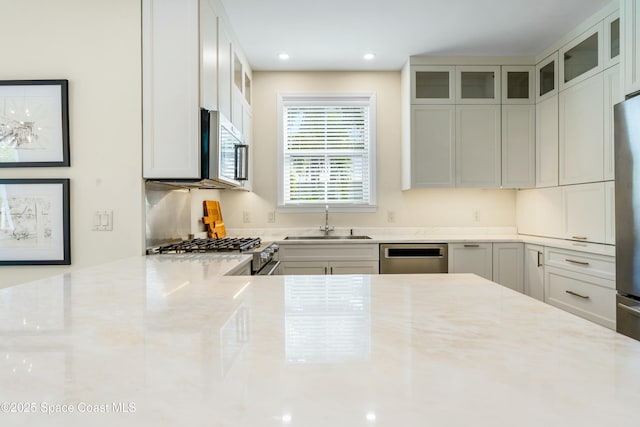 kitchen with light stone counters, recessed lighting, a sink, appliances with stainless steel finishes, and glass insert cabinets