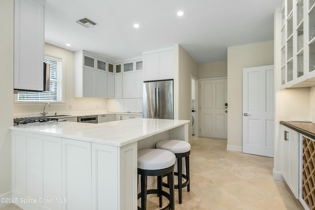 kitchen featuring recessed lighting, stainless steel appliances, a peninsula, visible vents, and a kitchen bar