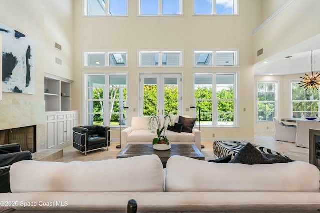 living area featuring visible vents, a premium fireplace, french doors, built in shelves, and a chandelier