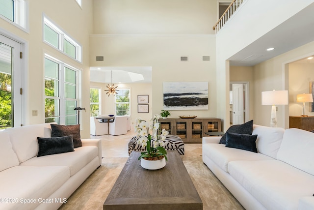 living area with a wealth of natural light, a high ceiling, visible vents, and an inviting chandelier