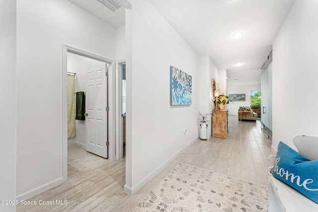 hallway with baseboards, visible vents, and light wood finished floors