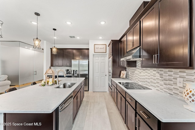 kitchen with hanging light fixtures, appliances with stainless steel finishes, a sink, dark brown cabinets, and under cabinet range hood