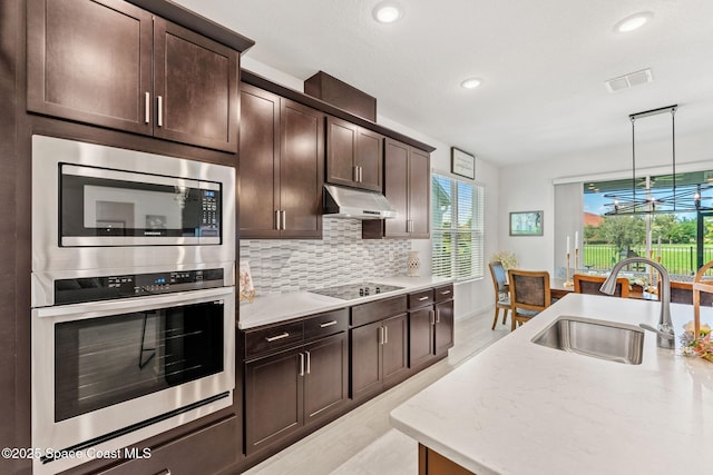 kitchen with under cabinet range hood, stainless steel appliances, a sink, visible vents, and decorative backsplash