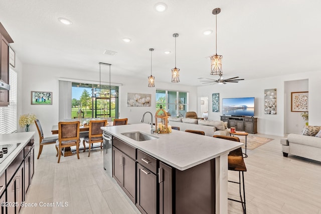 kitchen with a breakfast bar area, stainless steel dishwasher, open floor plan, dark brown cabinetry, and a sink