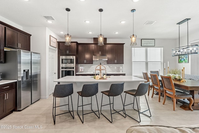 kitchen with appliances with stainless steel finishes, light countertops, visible vents, and a kitchen breakfast bar