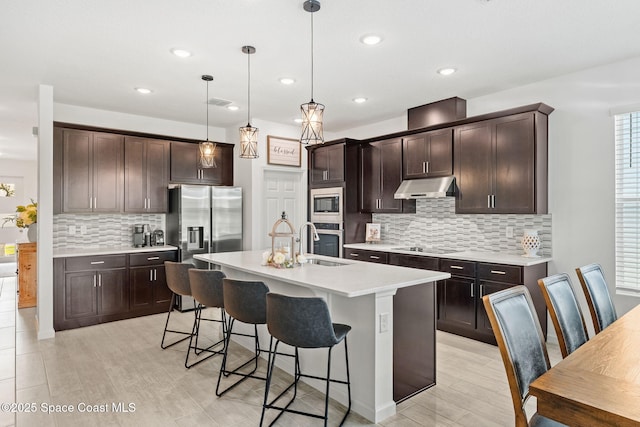 kitchen with under cabinet range hood, appliances with stainless steel finishes, dark brown cabinets, and a breakfast bar area