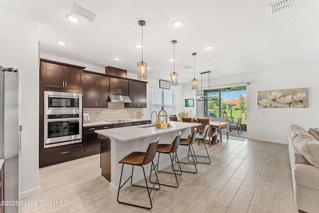 kitchen with under cabinet range hood, visible vents, appliances with stainless steel finishes, backsplash, and a kitchen bar