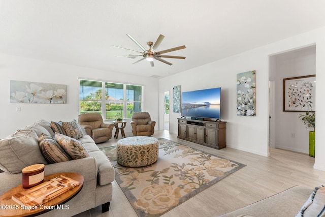 living area featuring a ceiling fan, baseboards, and light wood finished floors