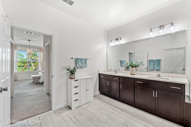 ensuite bathroom featuring wood finished floors, visible vents, a sink, and double vanity