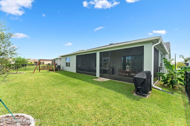 back of property featuring a playground, a yard, stucco siding, a sunroom, and fence