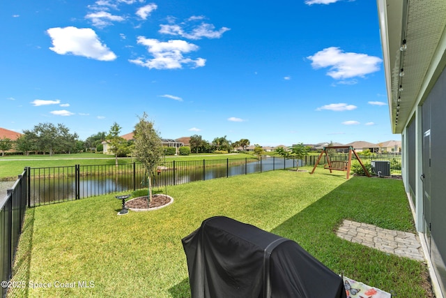 view of yard with a water view, a fenced backyard, a playground, and central AC