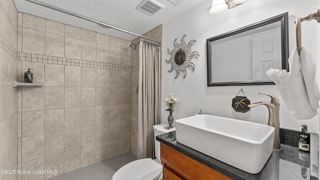 bathroom with visible vents, toilet, a tile shower, vanity, and a textured ceiling