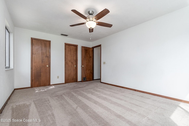 unfurnished bedroom featuring light carpet, multiple closets, visible vents, and baseboards