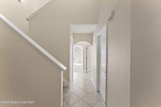 hall with arched walkways, stairway, baseboards, and light tile patterned floors