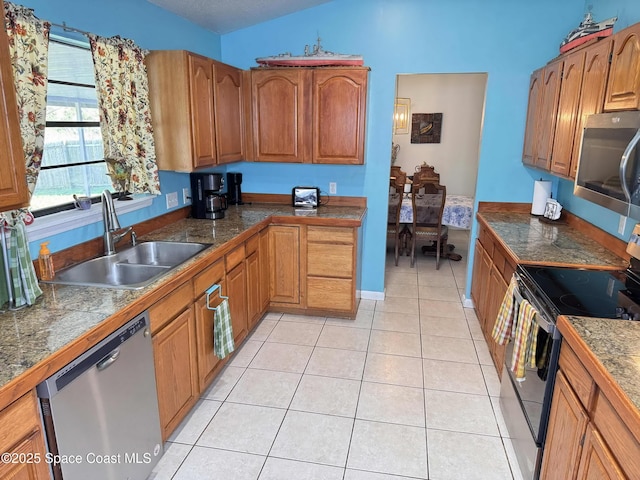 kitchen featuring light tile patterned floors, a sink, vaulted ceiling, appliances with stainless steel finishes, and brown cabinetry