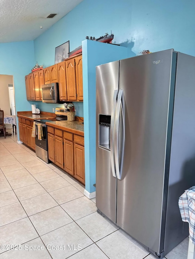 kitchen featuring stainless steel appliances, visible vents, brown cabinetry, light tile patterned flooring, and a textured ceiling