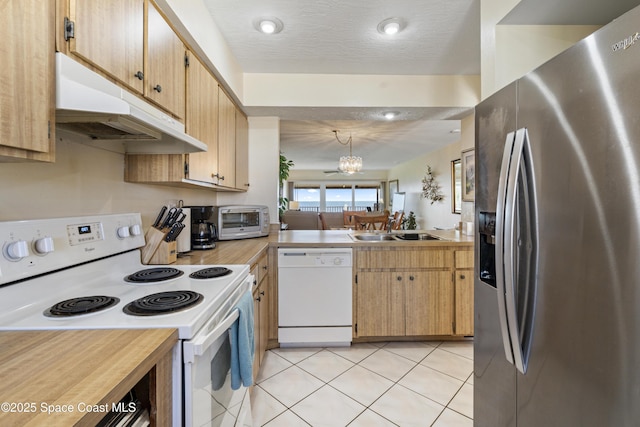 kitchen with white appliances, under cabinet range hood, light countertops, and a sink