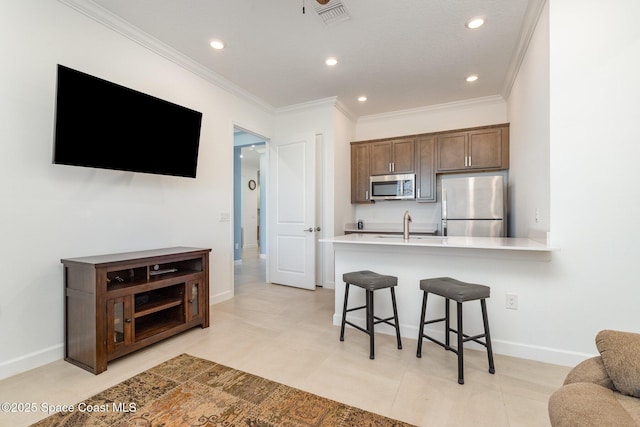 kitchen with visible vents, ornamental molding, light countertops, appliances with stainless steel finishes, and a kitchen breakfast bar