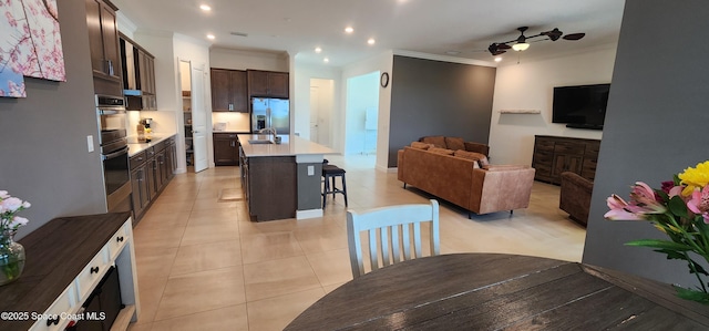 kitchen with dark brown cabinets, open floor plan, a kitchen breakfast bar, stainless steel fridge, and a sink