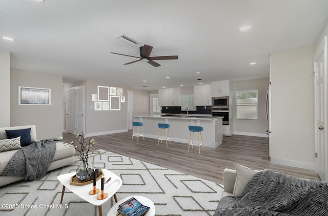 living area featuring light wood finished floors, recessed lighting, visible vents, ceiling fan, and baseboards