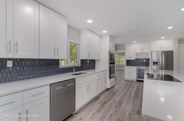 kitchen with wine cooler, appliances with stainless steel finishes, light countertops, white cabinetry, and a sink