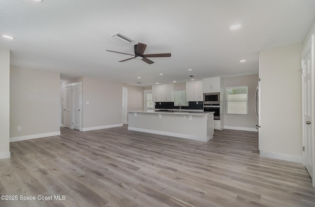 kitchen with light wood finished floors, appliances with stainless steel finishes, open floor plan, and a sink