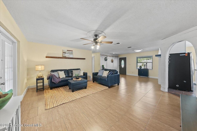 living area featuring baseboards, arched walkways, visible vents, and a textured ceiling