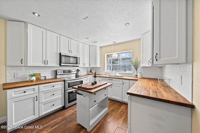 kitchen featuring dark wood finished floors, appliances with stainless steel finishes, white cabinets, wood counters, and a sink