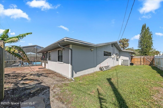 view of side of property with glass enclosure, a yard, and a fenced backyard