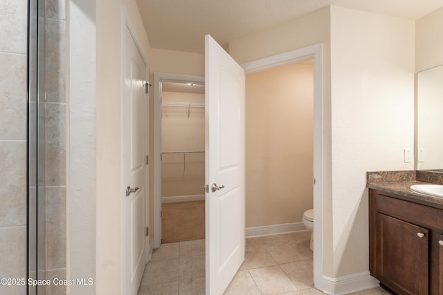 bathroom featuring tile patterned flooring, toilet, vanity, baseboards, and a walk in closet