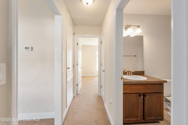 corridor featuring light carpet, a sink, and baseboards