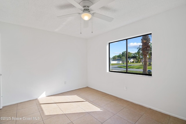 spare room with a ceiling fan, light tile patterned flooring, a textured ceiling, and baseboards