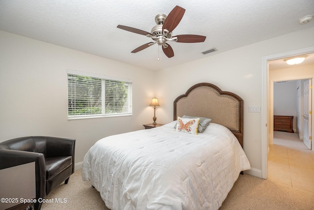 bedroom featuring light tile patterned floors, a textured ceiling, light carpet, visible vents, and a ceiling fan