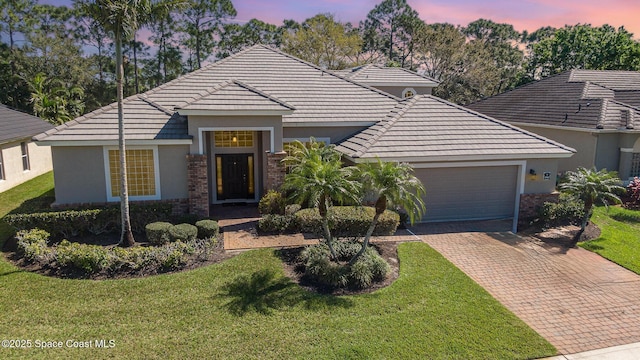 view of front of house featuring a garage, decorative driveway, brick siding, and a lawn