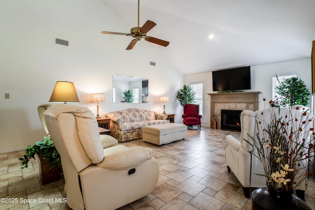 living room featuring visible vents, a tiled fireplace, a ceiling fan, stone finish floor, and high vaulted ceiling