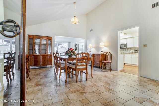 dining area featuring baseboards, high vaulted ceiling, visible vents, and an inviting chandelier