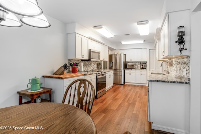 kitchen with light wood finished floors, decorative backsplash, stainless steel appliances, white cabinetry, and a sink