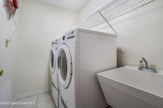 washroom with laundry area, light tile patterned floors, baseboards, washing machine and dryer, and a sink