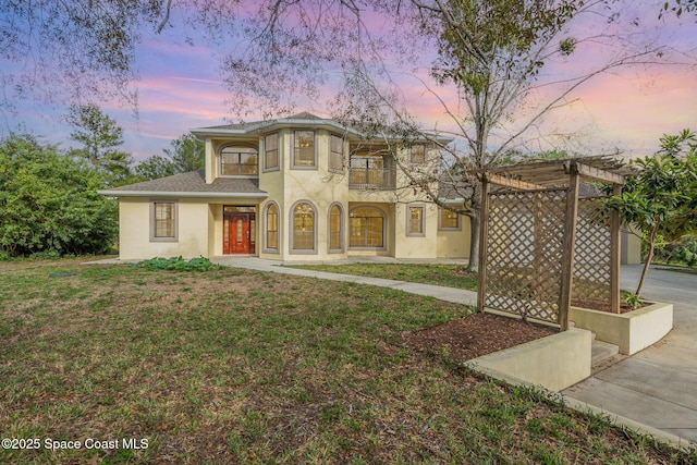 mediterranean / spanish house with a balcony, concrete driveway, a lawn, stucco siding, and a pergola