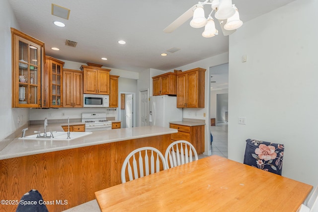 kitchen with white appliances, visible vents, brown cabinetry, glass insert cabinets, and a peninsula