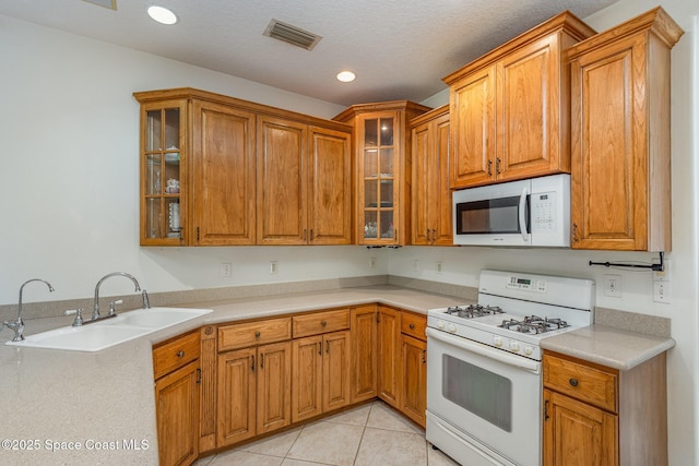 kitchen featuring white appliances, light tile patterned floors, visible vents, brown cabinets, and a sink