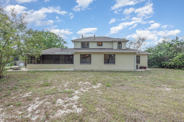 rear view of house featuring a sunroom, stucco siding, and a yard