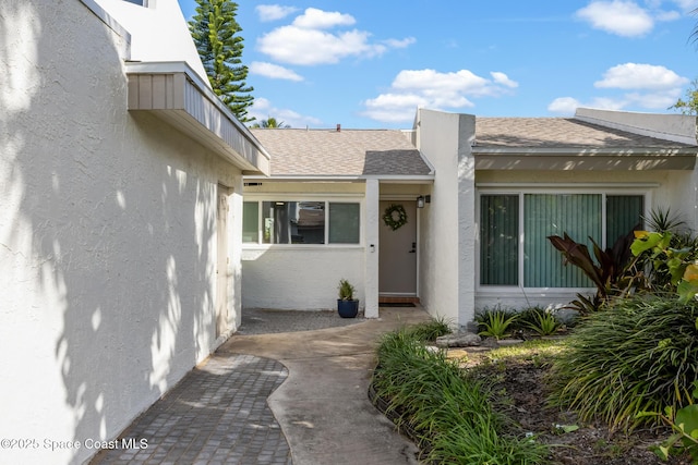 property entrance with roof with shingles and stucco siding