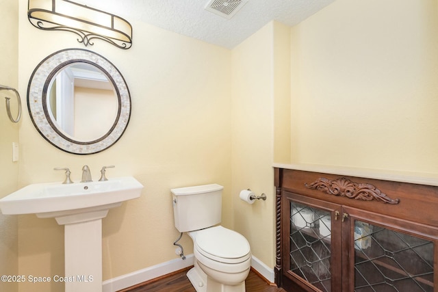 bathroom featuring wood finished floors, baseboards, visible vents, a textured ceiling, and toilet