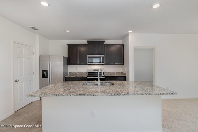 kitchen with stainless steel appliances, a sink, light stone counters, a center island with sink, and recessed lighting