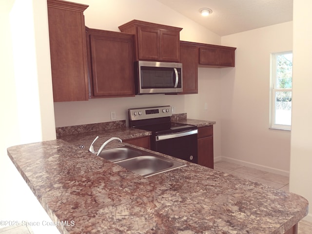 kitchen featuring lofted ceiling, appliances with stainless steel finishes, light tile patterned flooring, a sink, and a peninsula