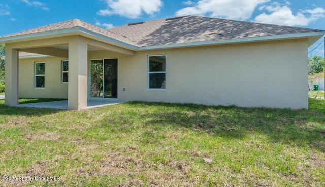 back of house with a patio area, a shingled roof, a lawn, and stucco siding