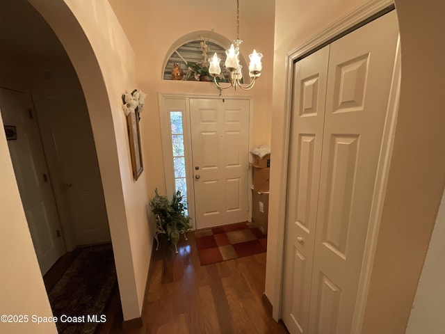 foyer entrance with arched walkways, dark wood-type flooring, and an inviting chandelier