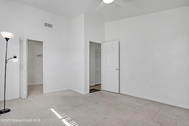 unfurnished bedroom with a walk in closet, visible vents, a towering ceiling, carpet flooring, and baseboards