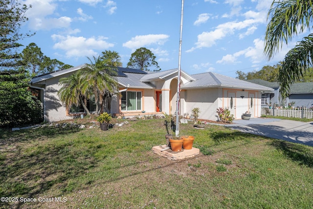 view of front of home with stucco siding, roof mounted solar panels, metal roof, fence, and a front lawn